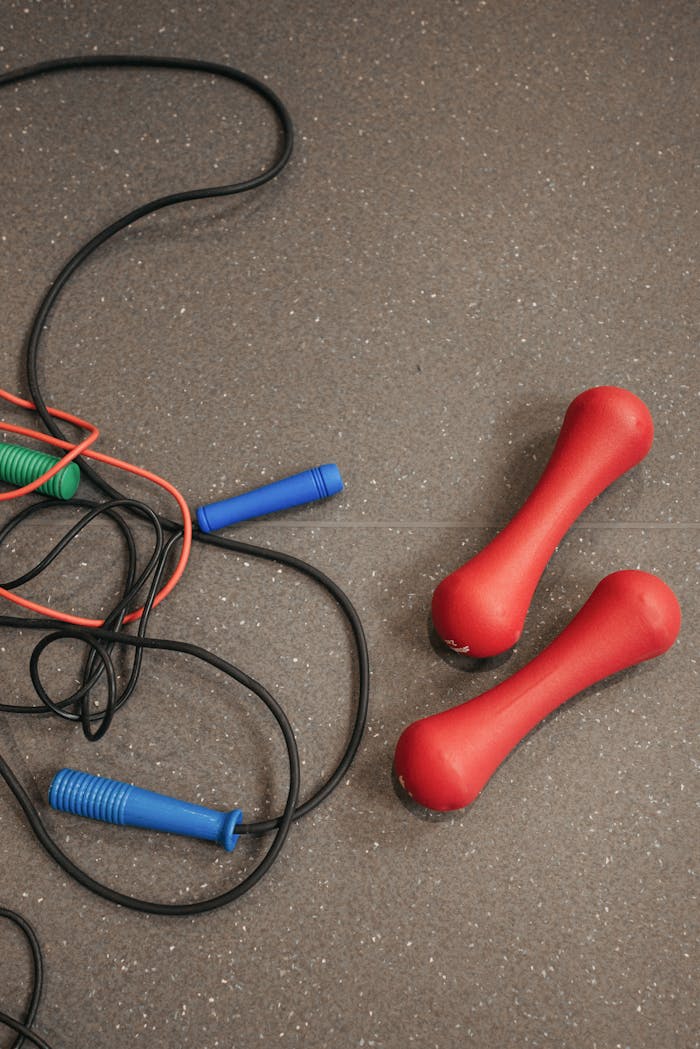 Red dumbbells and jump ropes on a textured tile floor, ideal for fitness themes.